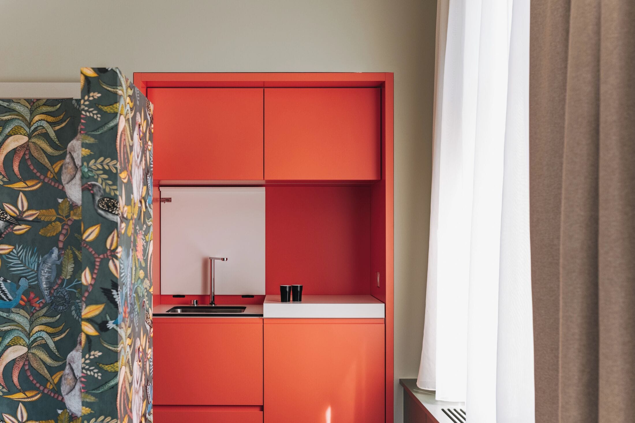 A room with a red cabinet, a white countertop, and a patterned curtain.