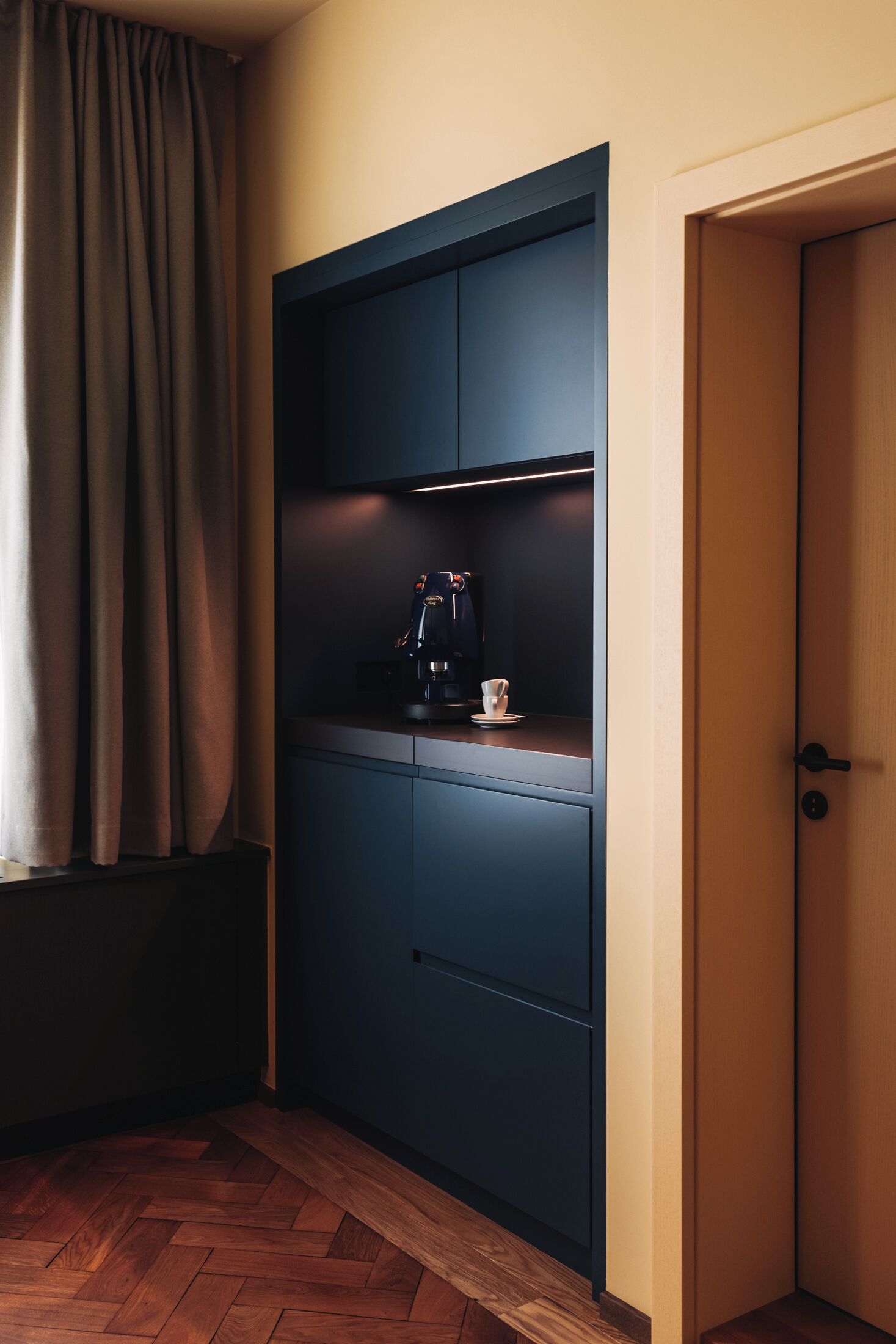 A room with a dark blue wardrobe, a coffee machine, and a cup on the counter.
