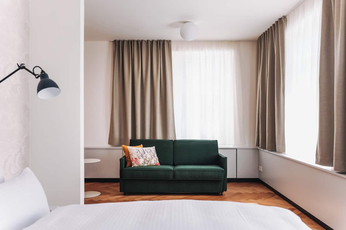 Une pièce avec un lit, un canapé vert, une lampe et une fenêtre avec des rideaux.