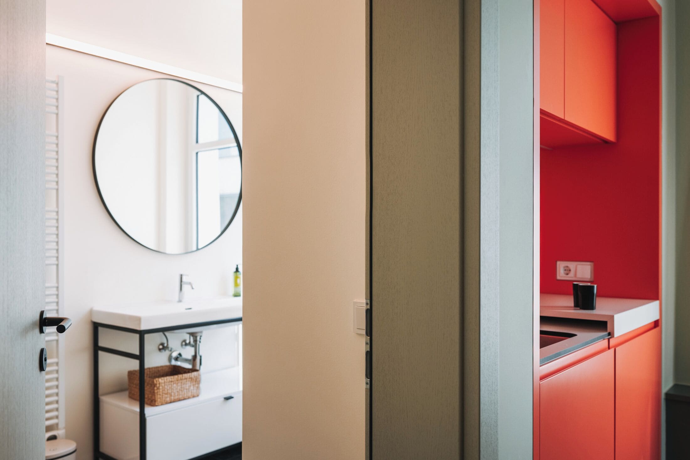Ein modernes Badezimmer mit einem weißen Waschbecken, einem runden Spiegel und einer roten Akzentwand.