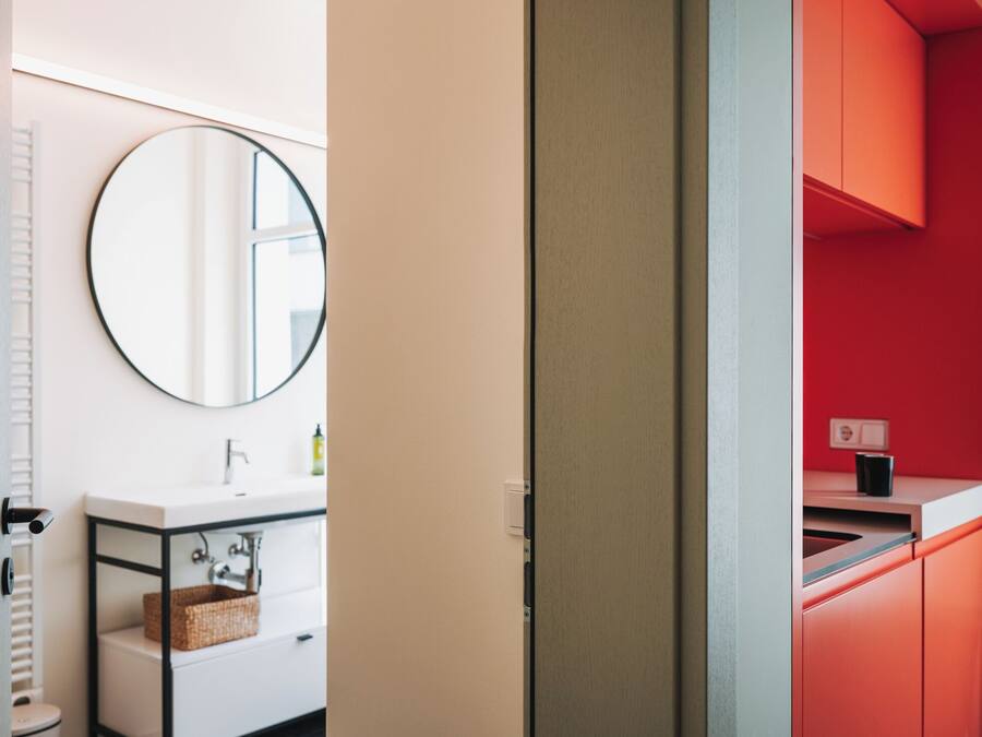 Ein modernes Badezimmer mit einem weißen Waschbecken, einem runden Spiegel und einer roten Akzentwand.