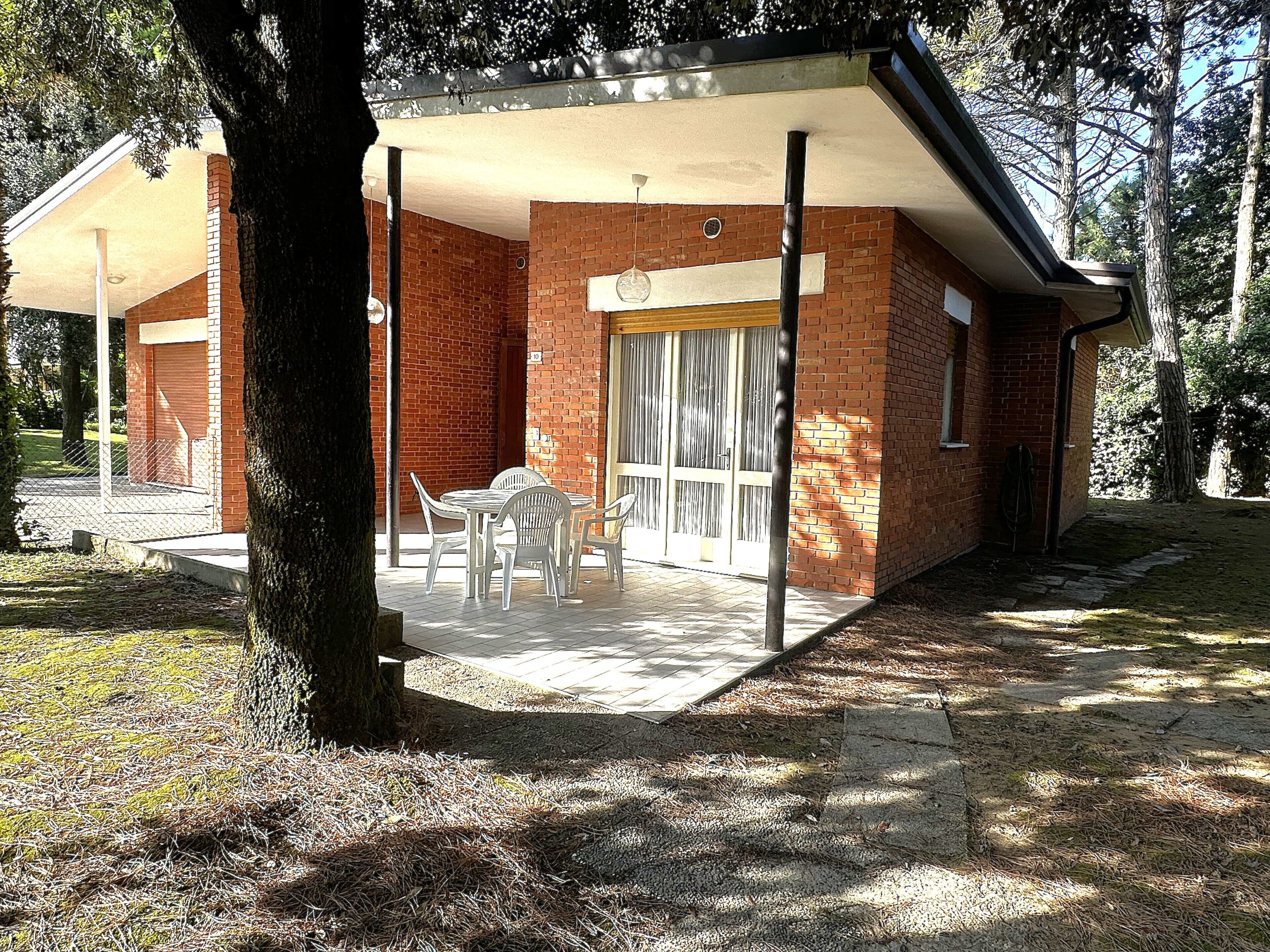 Un edificio in mattoni con un portico coperto, un tavolo e sedie, e un'ampia finestra.