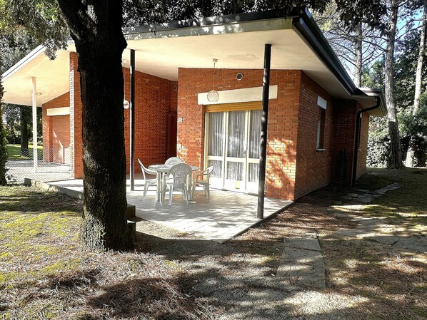 A brick building with a covered patio, a table and chairs, and a large window. - Relaxing Villa With Garden Surrounded by Nature (San Michele al Tagliamento)