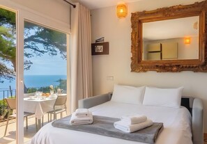 Een hotelkamer met een bed, een grote spiegel, een tafel met stoelen en uitzicht op zee.