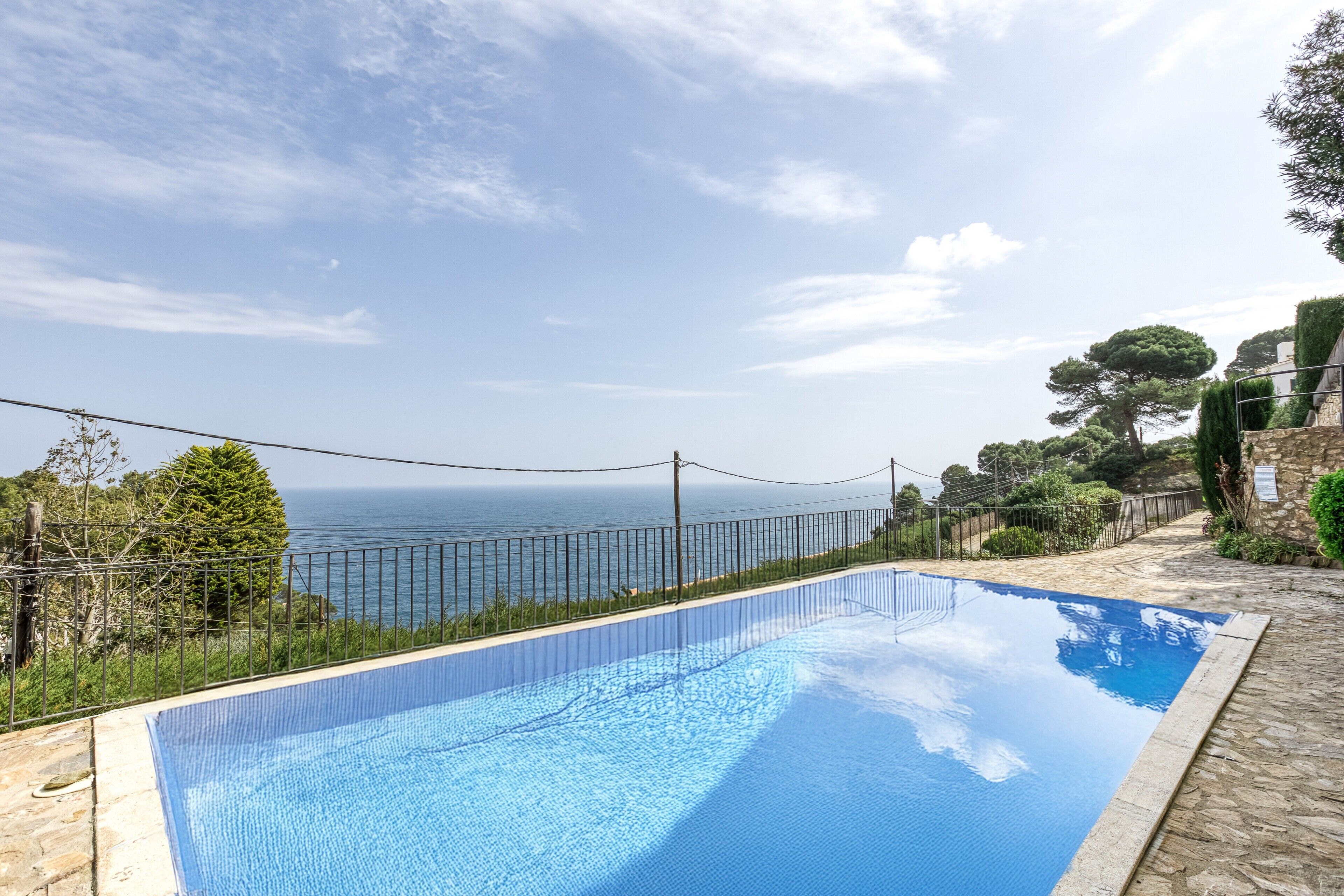 A swimming pool with a view of the sea, surrounded by stone walls and greenery.