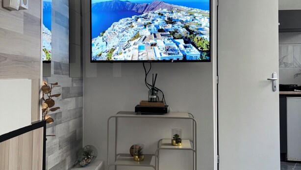 A modern living room with a flat-screen TV mounted on the wall, a minimalist console table with decorative items, and a marble floor. - Le Darcy / DIJON train station and city center (Dijon)