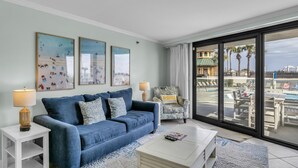 Una sala de estar con un sofá azul, una mesa de centro blanca y un sillón con un cojín.
