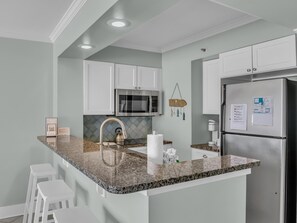 Une cuisine moderne avec des meubles blancs, un plan de travail en granit, des appareils électroménagers en acier inoxydable et un petit îlot central avec des tabourets.