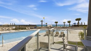 Zona de piscina con barandilla de cristal, sillas de descanso y vista a la playa.