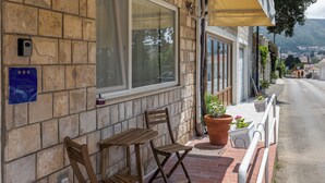 A stone building with a sign indicating it is a studio apartment. There are two wooden chairs and a table outside, with a yellow awning above. - Sunny Palace Studio 3 (Dubrovnik)