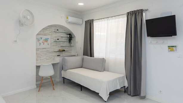 A modern living room with a sofa, a white chair, a TV, and a fan. - Sunny Palace Studio 3 (Dubrovnik)