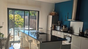 Una cuina moderna amb una illa central, tamborets de bar, un frigorífic i vistes a l'exterior.