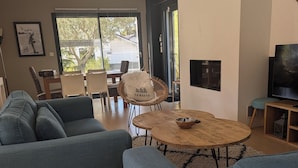 Un saló modern amb un sofà gris gran, una taula de centre de fusta, i una cadira de vimet. Hi ha una televisió sobre un suport de fusta i una fotografia amb marc a la paret.