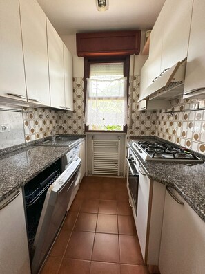 A compact kitchen with white cabinets, a gas stove, a built-in oven, and a dishwasher. - Quiet Gardened Villa for six Guests Near the sea (San Michele al Tagliamento)