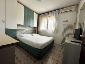Et lille hotelværelse med en enkelt seng, et skrivebord, et skab og en radiator.