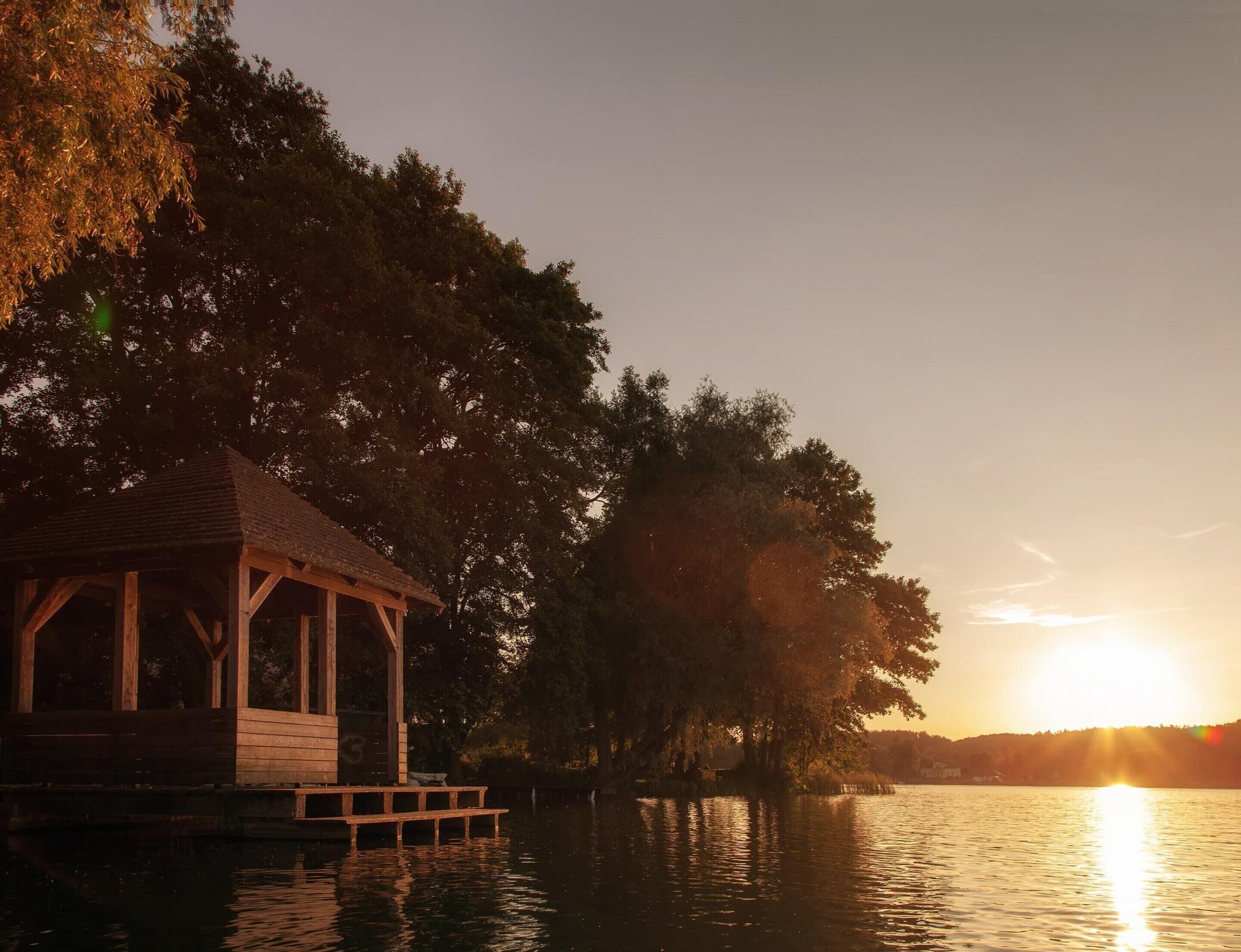 Un gazebo di legno di fronte a un lago calmo al tramonto.