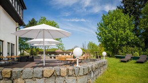 An outdoor patio area with stone walls, tables, chairs, and umbrellas. - Kaiserhof Feldberg by Belvilla Resorts-twin Room (Feldberger Seenlandschaft)