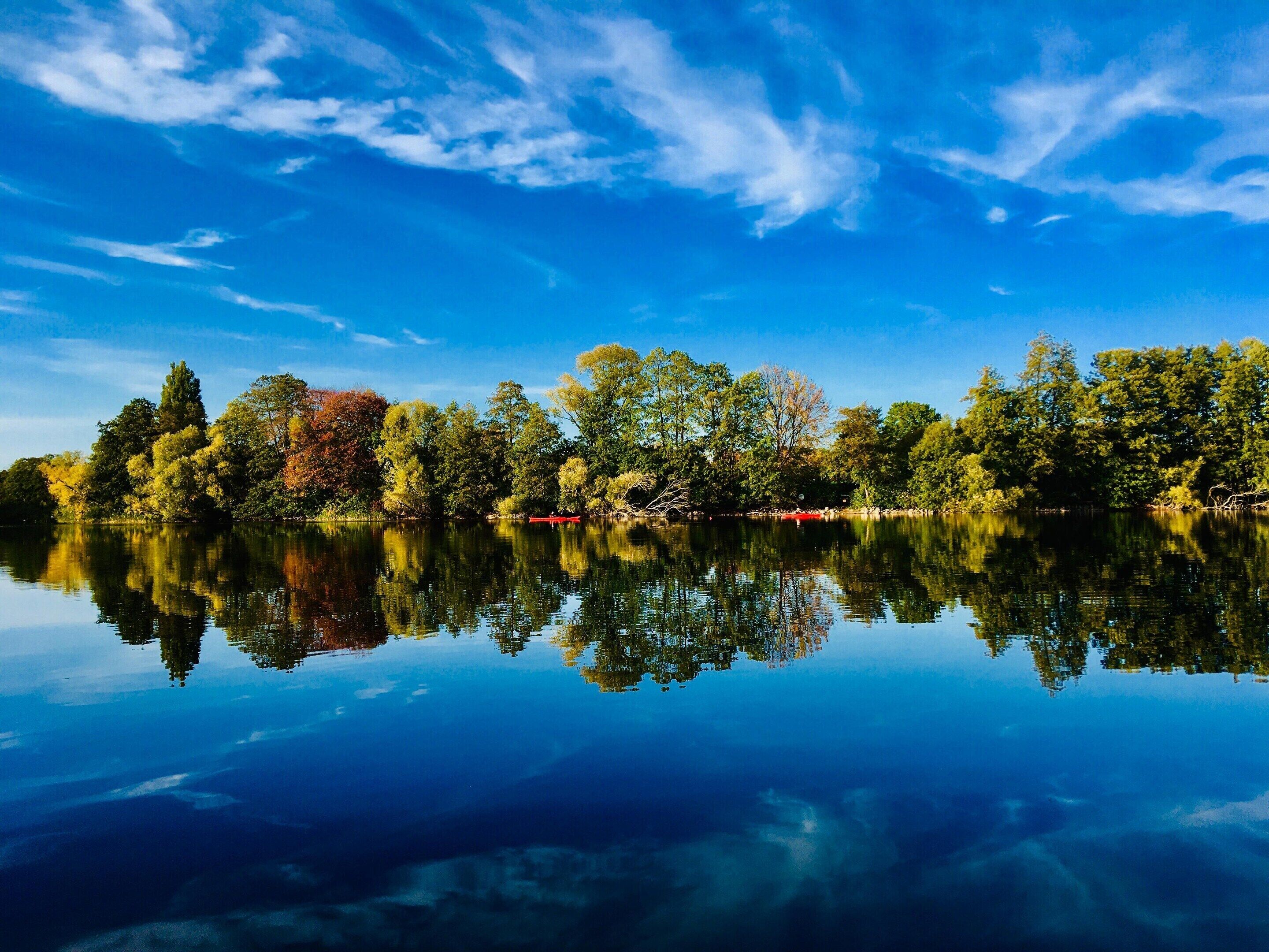 Un lago tranquilo con árboles reflejados en el agua, un cielo despejado y un bote rojo.