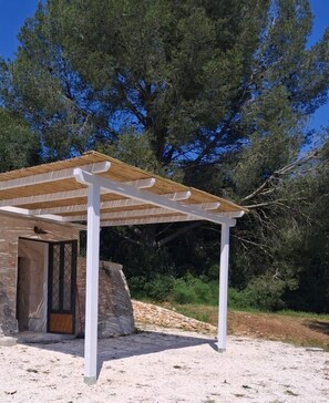 A covered outdoor area with a stone wall, a wooden door, and a white pergola structure. - Ancient Saracen Trullo from the 1700s nestled in the green of Puglia's centuries-old olive grove (ostuni)