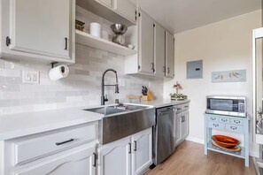 Cozinha moderna com armários brancos, eletrodomésticos de aço inoxidável e um micro-ondas em um armário azul claro.