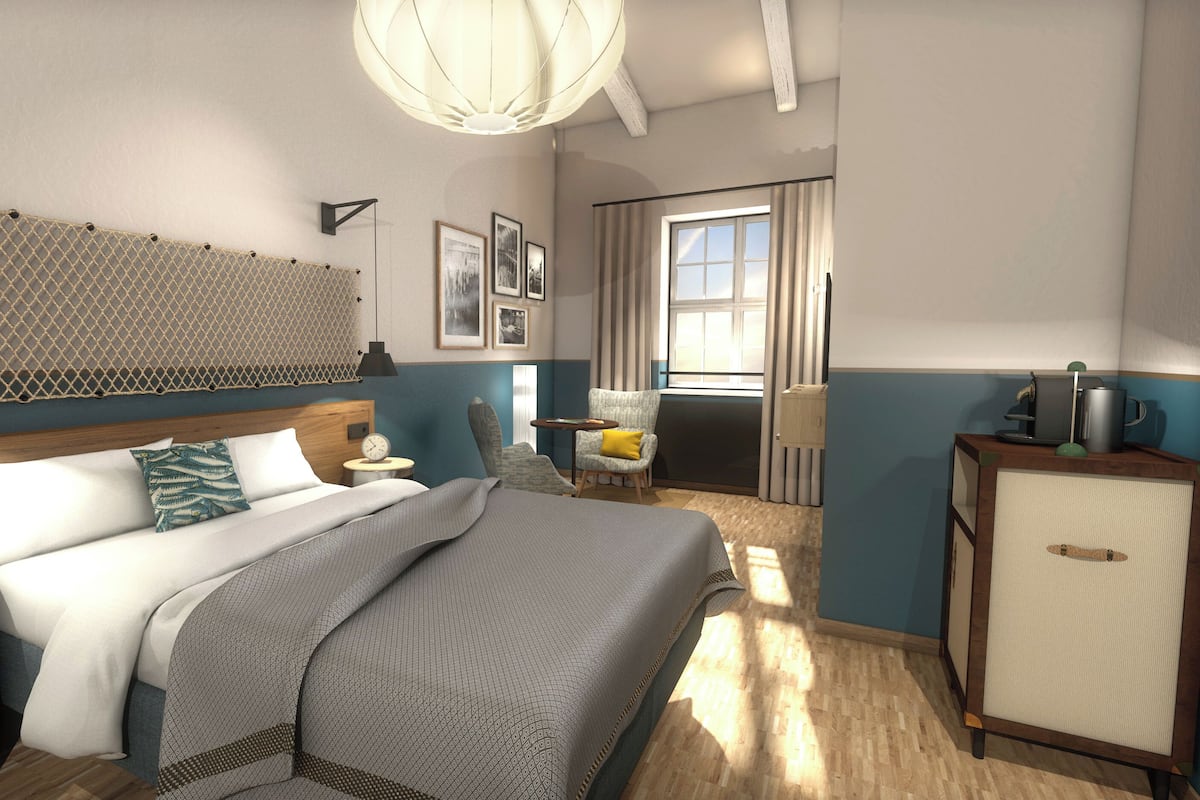 Moderni hotellihuone, jossa on sänky, yöpöydät, tuoli, työpöytä, vaatekaappi ja suuri ikkuna.