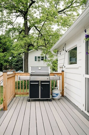 Eine Terrasse mit Grill, Propangasflasche und einem Haus im Hintergrund.