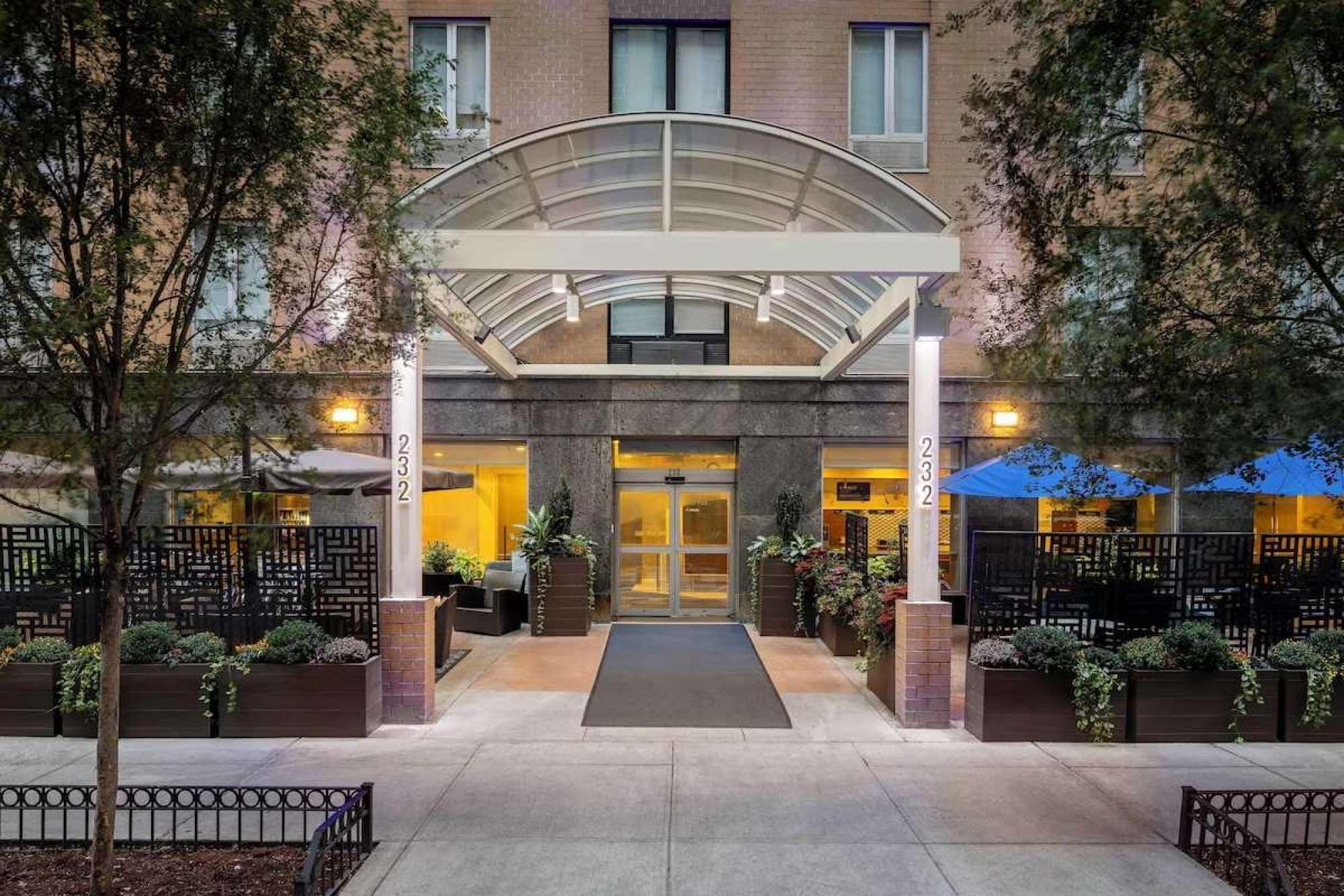 A hotel entrance with a covered walkway, outdoor seating, and a number '232' on the pillars.