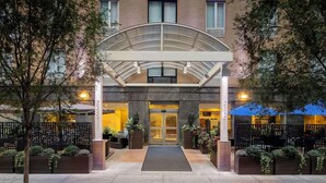 A hotel entrance with a covered walkway, outdoor seating, and a number '232' on the pillars. - Steps to Madison Square Garden + Free Breakfast (New York City)