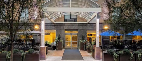 A hotel entrance with a covered walkway, outdoor seating, and a number '232' on the pillars.