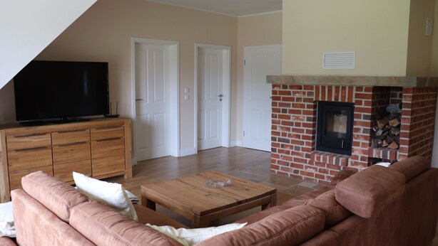 A living room with a flat-screen TV, a brick fireplace, a wooden coffee table, and a brown leather sofa. - Welcome to the Boskop vacation apartment (Stade)