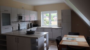 A modern kitchen with white cabinets, a microwave, and a sink. There's a dining table with chairs and a window providing a view of the outside. - Welcome to the Boskop vacation apartment (Stade)