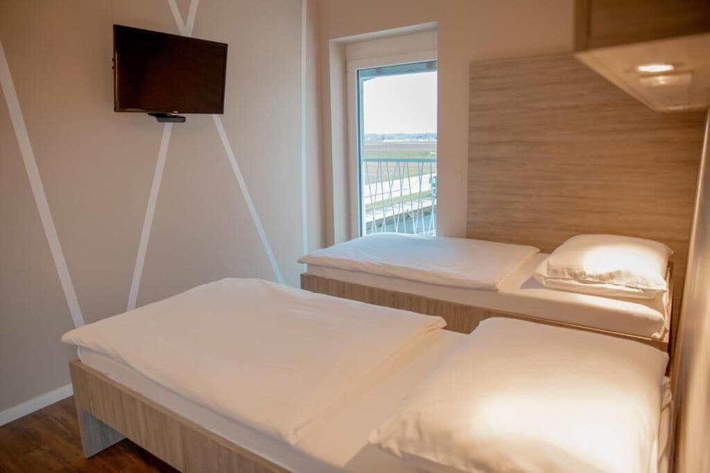 A bedroom with two beds, a TV mounted on the wall, and a window with a view of a bridge.