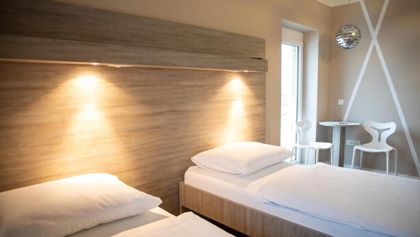 A modern hotel room with two beds, a wooden headboard, a small table, and white chairs. - Krško garni (Krsko)