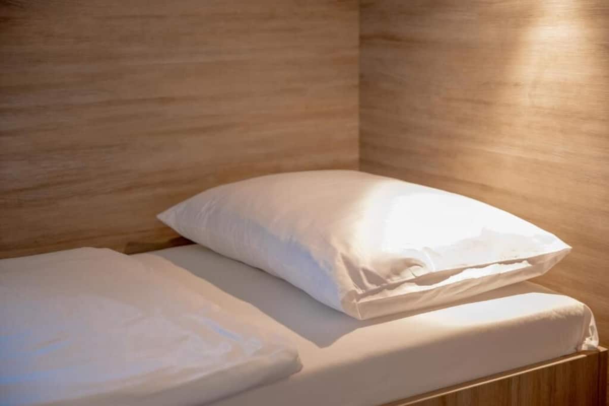 A neatly made bed with white linens and pillows in a room with wooden walls.