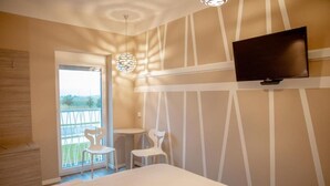 A hotel room with a bed, a TV mounted on the wall, a small table, two chairs, and a balcony with a view. - Krško garni (Krsko)