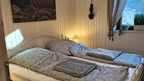 Un dormitorio con cama, un cuadro, lámpara colgante, ventana con cortinas y planta en maceta.