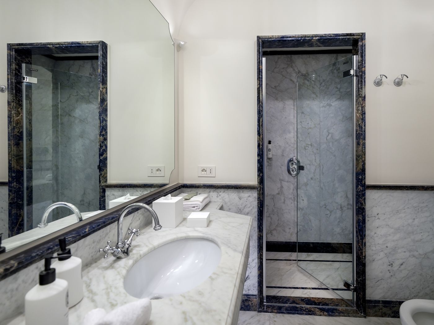 A modern bathroom with a marble sink, a large mirror, and a glass-enclosed shower.