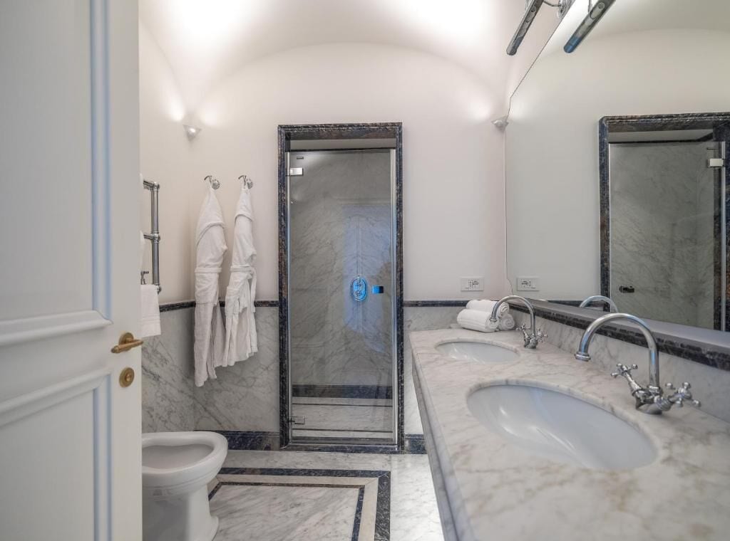 Un baño con ducha, dos lavamanos, inodoro y un espejo grande.