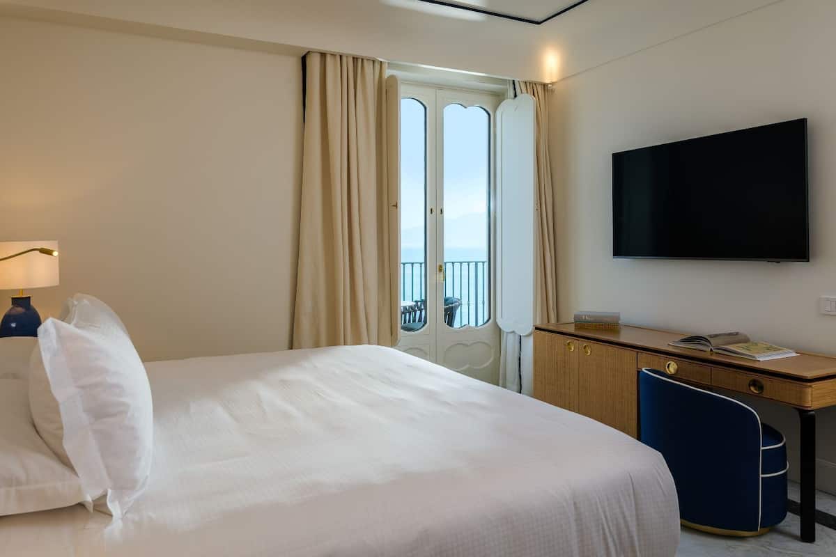 Habitación de hotel con cama, escritorio, silla, televisor y ventana con cortinas.