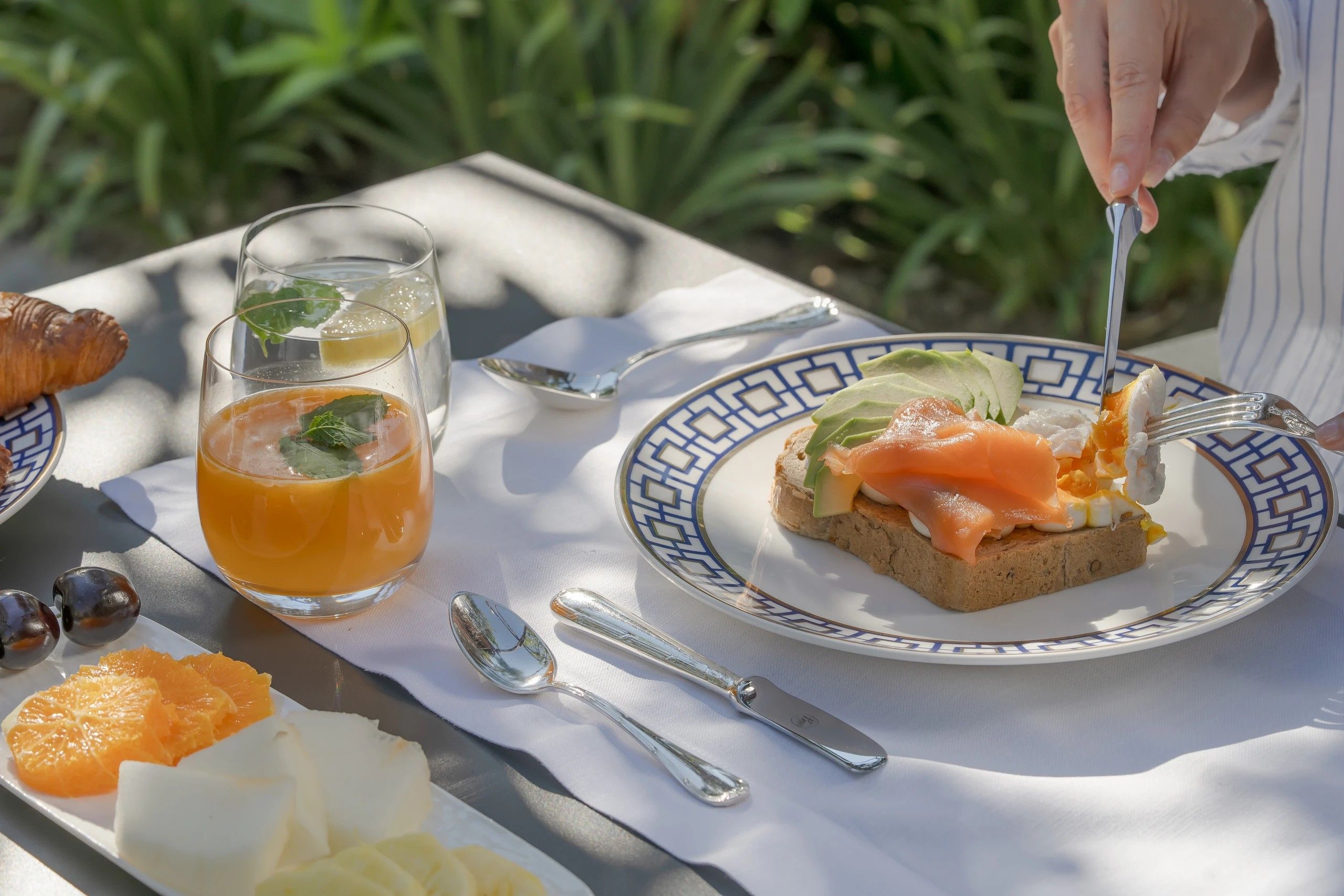 Un plato con salmón sobre tostada, un vaso de zumo de naranja y un croissant en una mesa.
