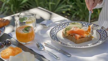 Un plato con salmón sobre tostada, un vaso de zumo de naranja y un croissant en una mesa.