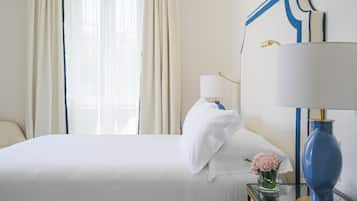 Quarto de hotel com cama, mesa de cabeceira, abajur, um vaso com flores e uma janela com cortinas.