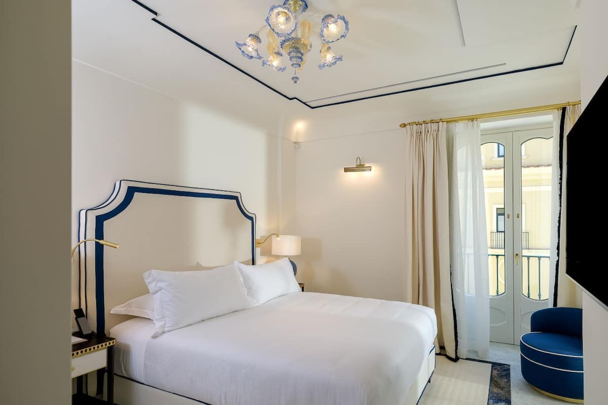 Habitación de hotel con una cama grande, un escritorio, una lámpara, un candelabro y vistas al exterior.