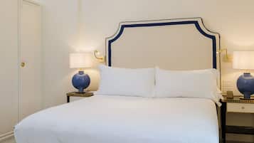Una cama bien tendida con cabecera, dos lámparas de noche y un candelabro.