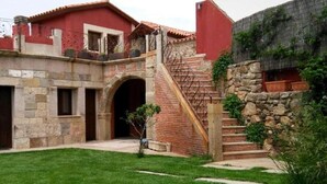 A courtyard with a stone staircase leading to a red building, a small tree, and a stone wall. - Tictágora House: House 2 (Plasenzuela)