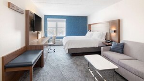 A hotel room with a bed, a desk, a sofa, a TV mounted on the wall, and a window with a view.
