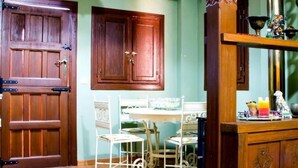 A room with two wooden doors, a white metal table with chairs, and a wooden cabinet with decorative items. - Tictágora House: House 3 (Plasenzuela)