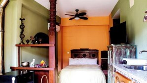 A bedroom with a bed, a ceiling fan, a television, and a kitchen area with a sink. - Tictágora House: House 3 (Plasenzuela)