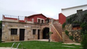 A pool with a stone border, a brick staircase, and a stone building with a red roof. - Tictágora House: House 3 (Plasenzuela)