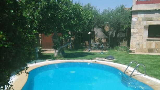 A swimming pool with a metal ladder, surrounded by greenery and a stone building. - Tictágora House: House 3 (Plasenzuela)